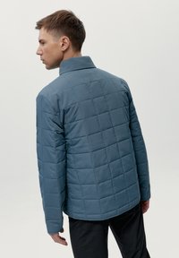 Chaqueta exterior acolchada azul con un alto cuello, que presenta un acabado texturizado y mangas largas, vista desde atrás sobre un fondo liso.