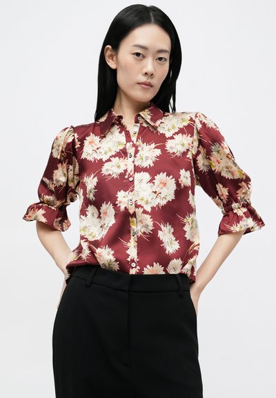 Bordó virágmintás blúz rövid puffos ujjakkal, gombos elülső résszel és enyhe fényességgel. A minta világos rózsaszín �és krém színű virágokat tartalmaz.