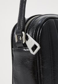 Borsa in pelle nera con finitura texturizzata, dotata di una cerniera argentata e di un'etichetta metallica con il nome del marchio. Tracolla liscia attaccata alla cerniera.