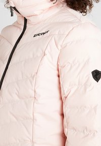 Růžová zateplená bunda s vodorovnými švy, vysokým límcem, předním zipem, černým logem na hrudi a značkovou nášivkou na rukávu.