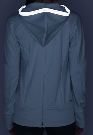 Personne portant un sweat à capuche bleu avec bordure réfléchissante sur la capuche, vue de dos en faible luminosité.