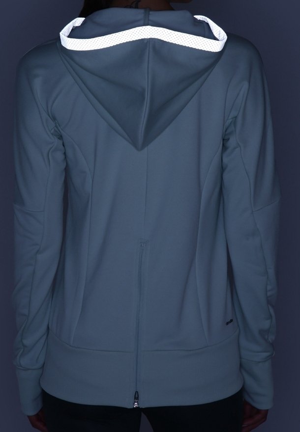 Personne portant un sweat à capuche bleu avec bordure réfléchissante sur la capuche, vue de dos en faible luminosité.