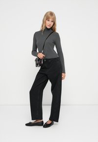 Hallamise turtleneck, must kõrge vöökoht ja laiad teksad, mustad lamedad kingad ning väike must ristiõlakott. Üksikasjalik taust.