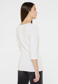 Weißes Baumwollhemd mit langen Ärmeln, rundem Ausschnitt und Dreiviertelärmeln. Verfügt über eine glatte Textur und eine figurbetonte Silhouette.