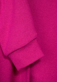 Tessuto di maglione fucsia con lavorazione a maglia texture. Presenta un dettaglio di polsini a costine, una superficie liscia e un colore vivace, senza pattern o accenti visibili.
