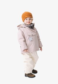 Dikke lichtroze jas met een sterdetail, grijze trui eronder, witte broek en bruine laarzen. Het kind draagt een oranje gebreide muts.