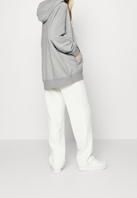 Sweatshirt à capuche gris avec une coupe décontractée, poches latérales et poignets côtelés, associé à un pantalon large blanc et des baskets blanches.