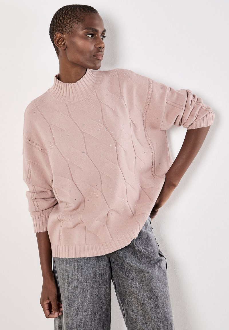 Hellrosa gestrickter Pullover mit hohem Rippkragen, strukturierten Wellenmustern und dezenten Verzierungen, kombiniert mit grauen weiten Hosen.