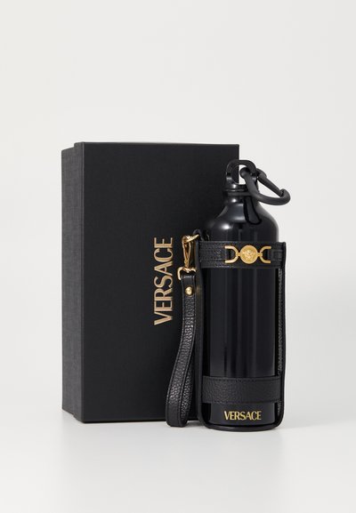 Bouteille d'eau isolée noire avec un support en cuir texturé et une sangle, dotée d'un logo Versace doré, emballée dans une boîte noire.