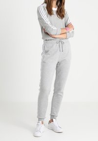 Sweat-shirt gris et pantalon de jogging en tissu doux, avec des rayures blanches le long des bras et des jambes, assortis à des baskets blanches.