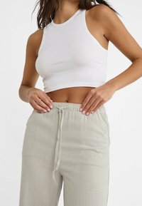 Hvid ribbet crop tank top parret med lysegrå drawstring bukser, der har en glat tekstur og løs pasform. Enkel design med minimale detaljer.