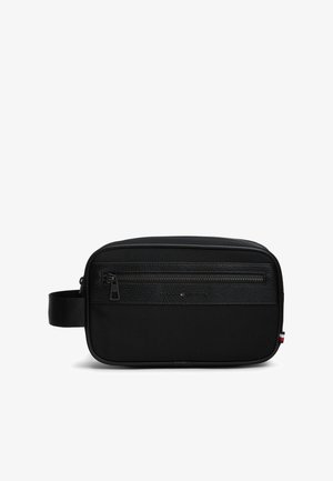 Trousse de toilette rectangulaire noire avec poche avant zippée, section supérieure texturée, poignée latérale et petite étiquette rouge, blanche et bleue sur le bord.