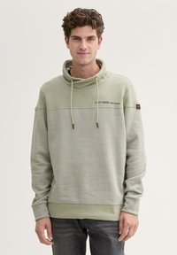 Felpa con cappuccio di colore verde chiaro, dotata di una parte superiore testurizzata, una sezione inferiore liscia in contrasto, cordini regolabili e dettaglio del logo sul petto.