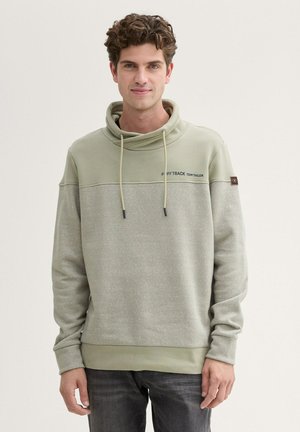 Bluza z kapturem w jasnym zielonym kolorze, z teksturowaną górną częścią, kontrastującą gładką dolną częścią, regulowanymi sznurkami oraz detalem logo na klatce piersiowej.