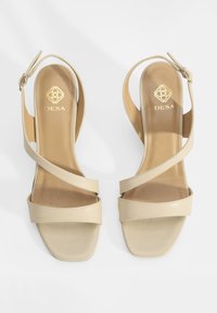 Sandales en cuir beige avec un bout carré, deux larges brides sur le dessus du pied et un design à talon ouvert. Comprend un logo doré sur la semelle intérieure.