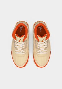 Ζευγάρι μπεζ και πορτοκαλί ψηλά sneakers με λευκά κορδόνια και λογότυπο Jumpman στη γλώσσα και την εσωτερική σόλα, απεικονιζόμενα από πάνω σε λευκό φόντο.