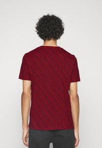 Camiseta corta de manga corta roja con un patrón espiral negro, cuello redondo y un corte relajado. La tela tiene una textura suave y un ligero estiramiento.