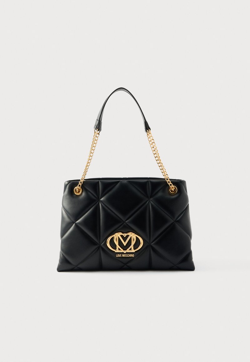 Μαύρη τσάντα tote από κεντημένο συνθετικό δέρμα με χρυσές αλυσίδες ως λουριά και έντονο χρυσό λογότυπο της μάρκας μπροστά. Διαθέτει απαλή υφή και δομημένο σχήμα.