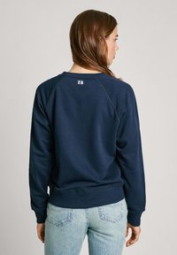 Felpa in cotone blu navy con maniche lunghe e spalle raglan, dotata di un piccolo logo sulla parte superiore della schiena e orlo a coste.