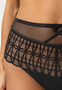Zwarte lingerie met een mesh ontwerp en fijne, ingewikkelde borduursels. Glad materiaal met een gegolfde rand en een elastische tailleband.