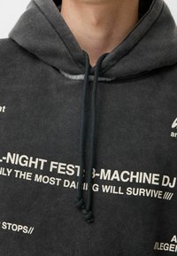 Sudadera con capucha de color gris oscuro con cordón, que presenta grandes textos y gráficos en blanco en la parte delantera. Tejido de mezcla de algodón con textura suave.