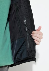 Schwarze wasserdichte Jacke mit Innenteil, das Etiketten für wasserabweisend, winddicht und atmungsaktiv enthält; glatte Textur mit Reißverschluss.