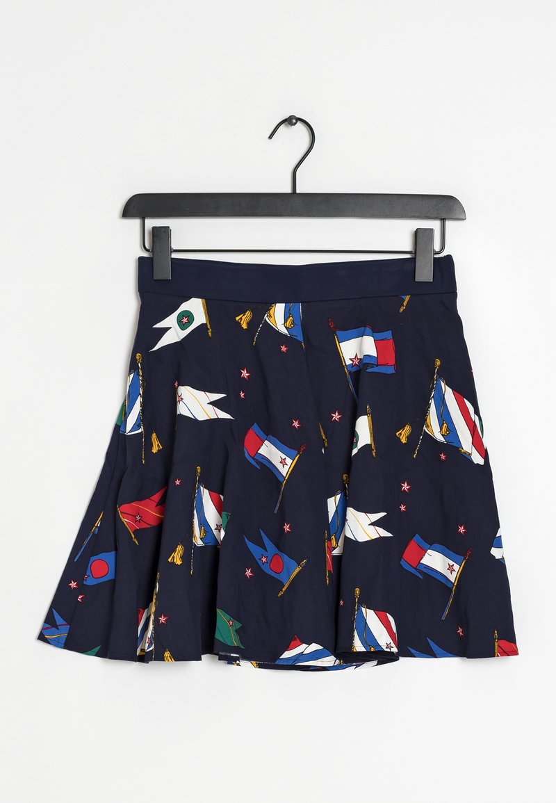 Jupe plissée bleu marine avec un motif de drapeaux nautiques colorés suspendue sur un cintre noir sur fond blanc.