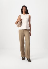 Lys beige ermeløs bluse med teksturert mønster, kombinert med beige vide bukser og mørke hælede sko. Bærer en liten beige veske.