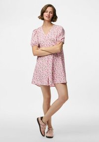 Růžové květinové šaty s krátkými nabíranými rukávy a výstřihem do V. Měkká látka, délka ke kolenům a pohodlný střih. Kombinováno s světle růžovými teniskami.