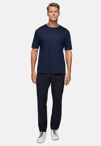 Navy short-sleeve t-shirt with a crew neck, paired with dark trousers and light-colored sneakers featuring gray laces.