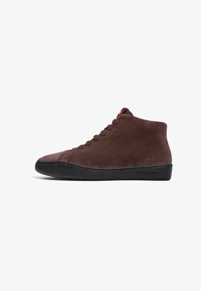 Brown suede high-top shoe with dark rubber sole, featuring six eyelets and a stitched design along the midsole. Red accent at the tongue.