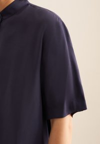 Maglietta blu navy a maniche corte con colletto a band, realizzata in tessuto liscio. Vestibilità leggermente morbida, con linee pulite e dettagli minimi.