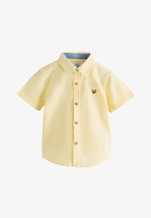 Chemise jaune pâle à manches courtes pour enfants, avec col et petit logo tête d'ours sur la poitrine gauche.