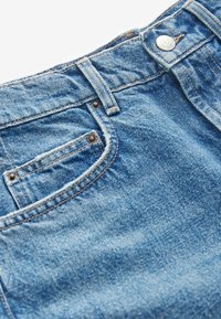Jean en denim bleu avec une finition délavée, doté d'une fermeture à bouton supérieur, d'une poche avant et de coutures contrastantes le long des coutures.
