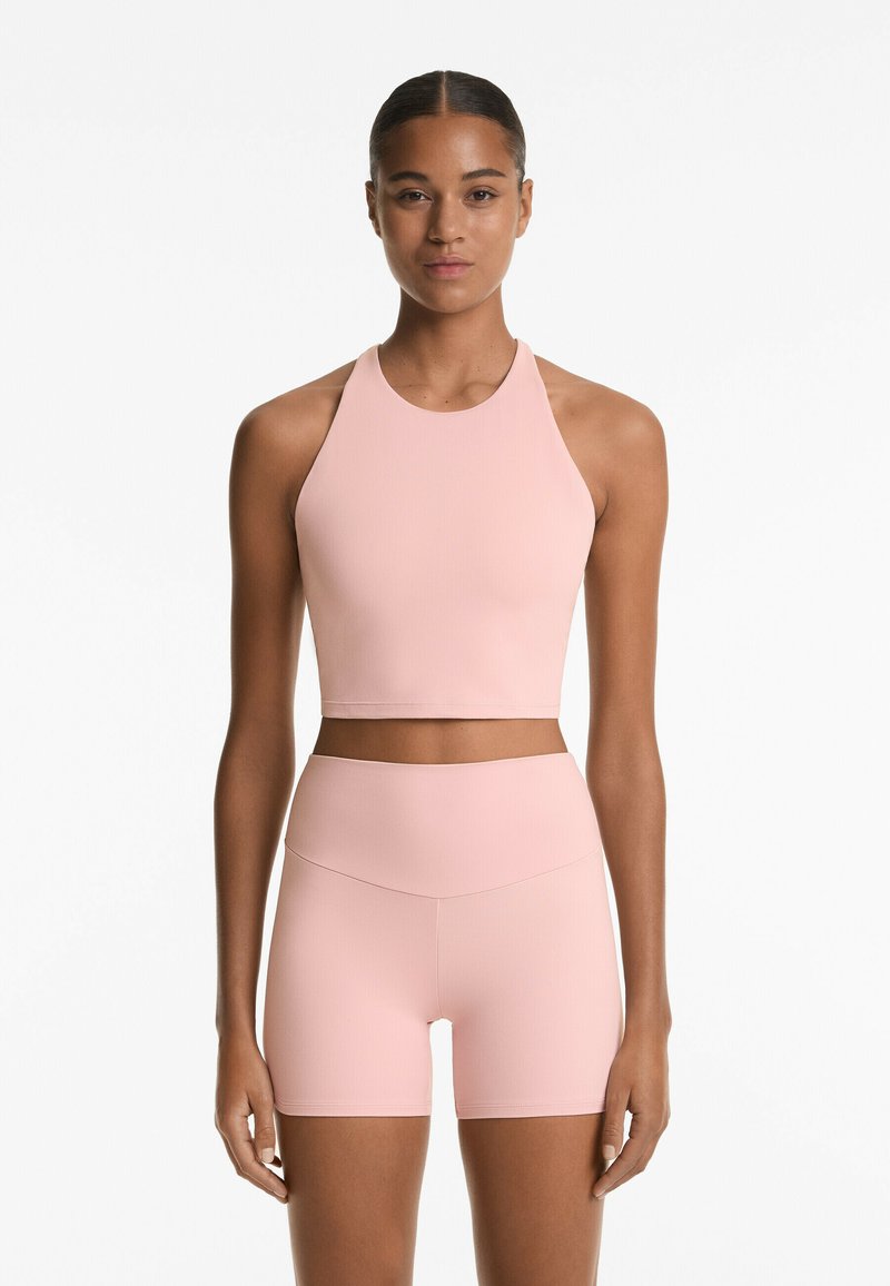 Világos rózsaszín sportos crop top, magas nyakkal, magas derékú, hozzá illő sorttal párosítva. Sima textúra, minimalista design.