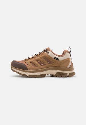 Brown hiking shoe featuring a mesh and suede upper, rubber toe cap, textured accents, and a thick white midsole. Lace-up design with loops.