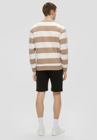 Pasiasty sweter w odcieniach beżu i bieli, wykonany z mieszanki bawełny, z okrągłym dekoltem i luźnym krojem. Połączony z czarnymi szortami i białymi trampkami.