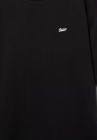 Schwarzer Pullover mit kleinem weißem "SWITZ"-Logo, das auf der oberen linken Brust aufgestickt ist.