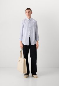 Lys blå skjorte med knapper, mørke bukser og en beige totebag. Uformelt mykt stoff, avslappet passform, en brystlomme og rullede ermer.