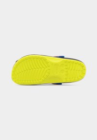 Κίτρινη σόλα παιδικού παπουτσιού τύπου κλογκ με μοτίβα πέλματος και ενδείξεις μεγέθους, ορατή από κάτω, σε απλό γκρι φόντο.