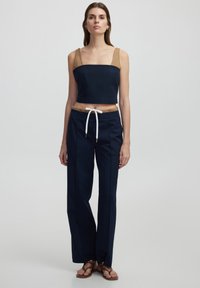Haut court navy avec des accents beige et des bretelles spaghetti ; associé à un pantalon large navy avec taille à cordon et détails blancs.