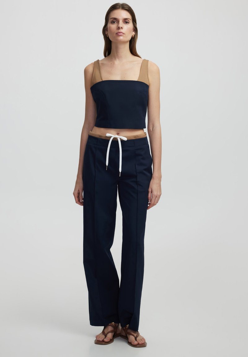 Haut court navy avec des accents beige et des bretelles spaghetti ; associé à un pantalon large navy avec taille à cordon et détails blancs.