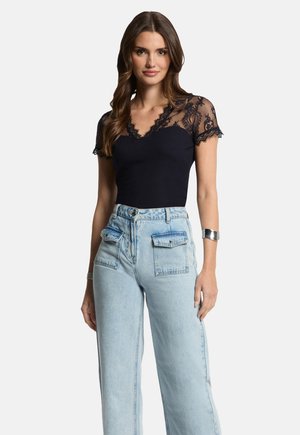 Navy top with short lace sleeves and V-neck; paired with high-waisted light blue wide-leg jeans featuring front pockets. Silver bracelet detail.