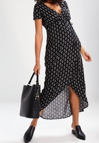 Robe à motif noir et blanc avec un décolleté en V, des manches courtes et un ourlet asymétrique. Associée avec un sac fourre-tout noir et des mules.