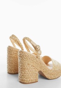 Sandales compensées beiges tissées avec des talons épais et texturés en tresse, design à bout ouvert et bride à la cheville avec une boucle.