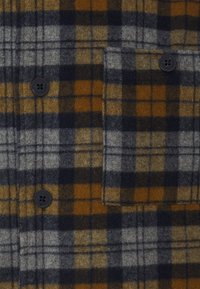 Flannel shirt featuring a plaid pattern in gray, navy, and mustard. Notable details include black buttons and a chest pocket. Soft texture.