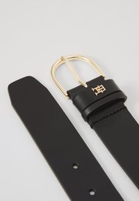 Black leather belt with a gold metal buckle and a brand logo detail, featuring a smooth texture and multiple adjustment holes.