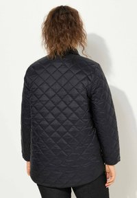 Chaqueta acolchada negra con un patrón de diamante, mangas largas y dobladillo recto. La tela tiene una textura suave y brillante.