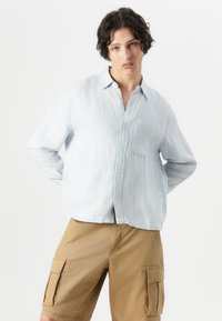 Light blue striped long-sleeve button-up shirt with a pocket. Paired with beige cargo shorts featuring side pockets and a relaxed fit.