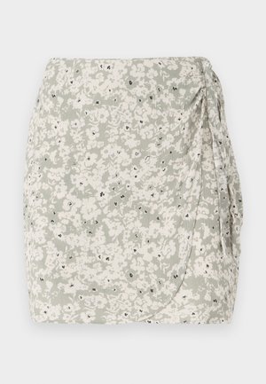 Világos zöld és krémszínű virágmintás mini szoknya, oldalt redőzéssel és fekete akcentus részletekkel. Puha, texturált anyag, amely becsomagolós dizájnnal rendelkezik.